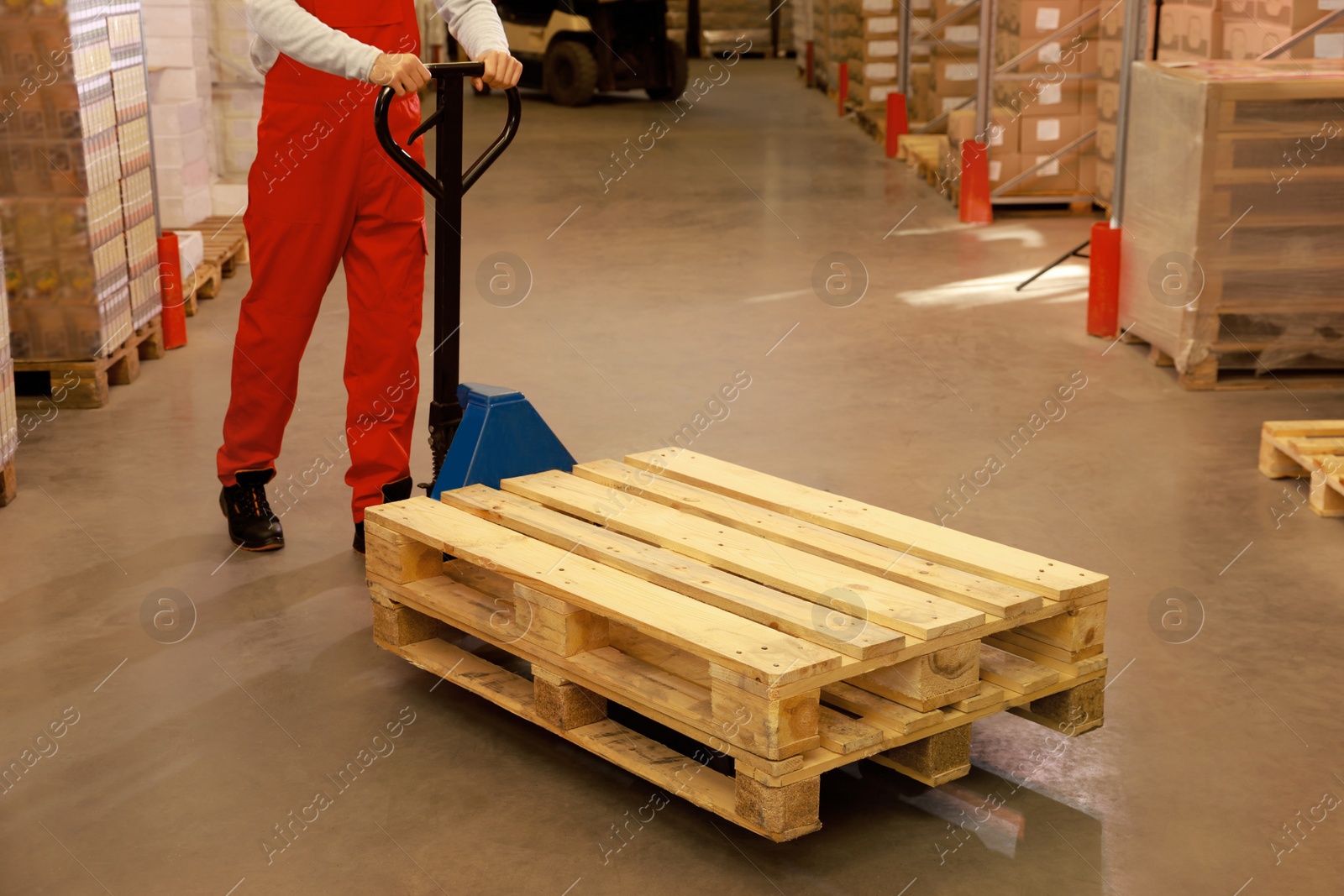 Image of Worker moving wooden pallets with manual forklift in warehouse, closeup