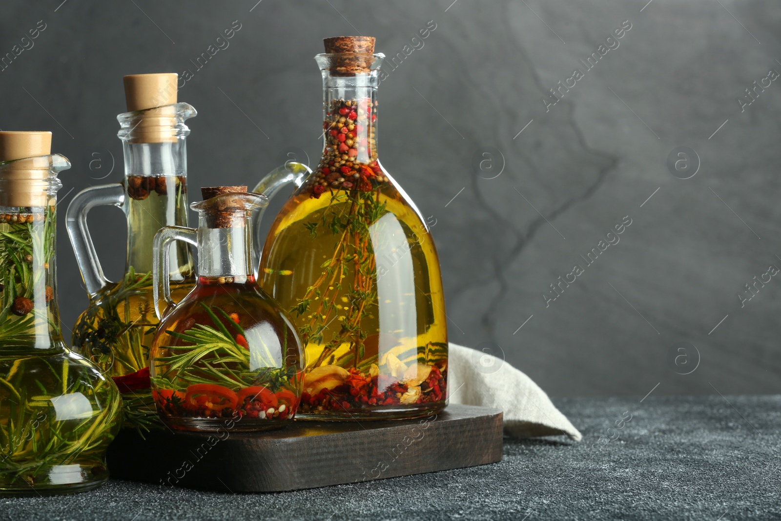 Photo of Cooking oil with different spices and herbs in jugs on light grey table. Space for text