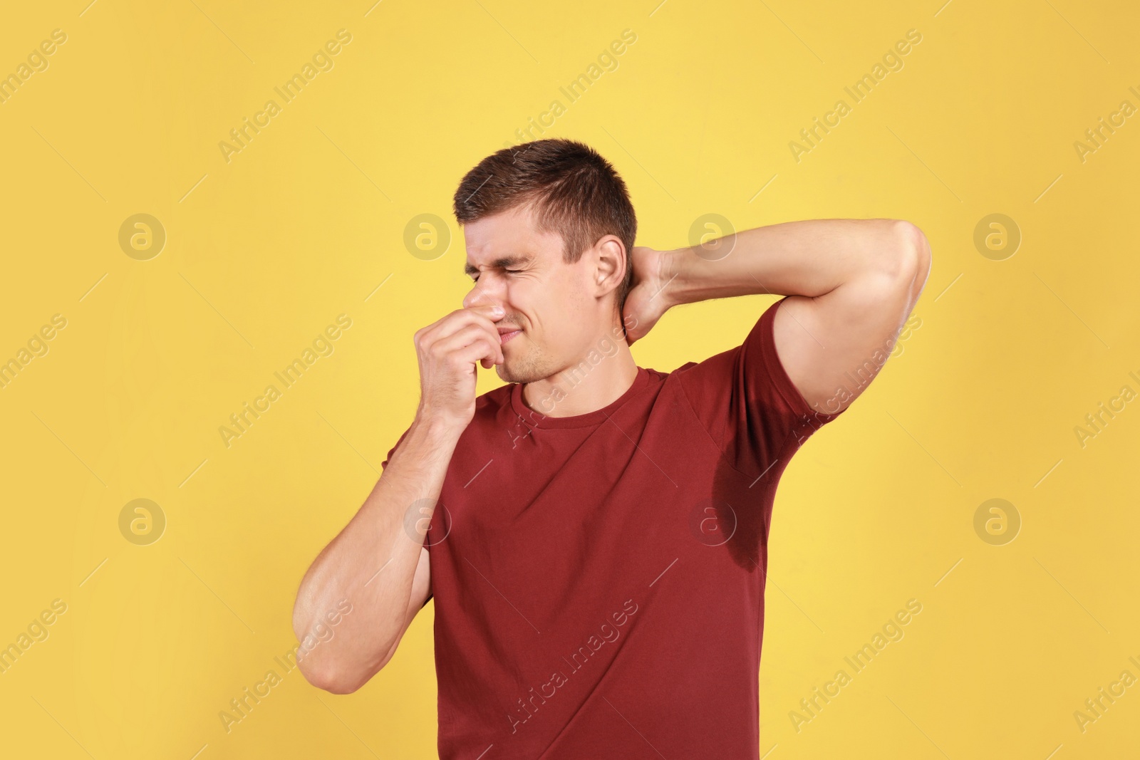 Photo of Young man with sweat stain on his clothes against yellow background. Using deodorant