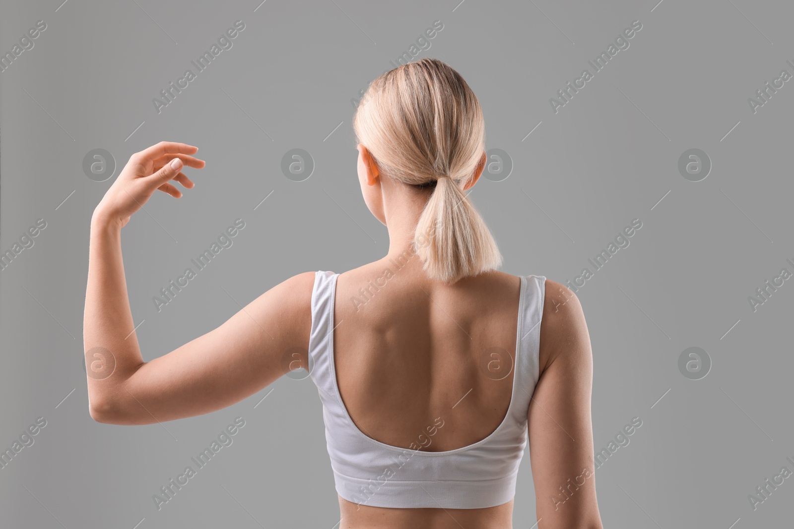 Photo of Woman showing her sporty body on grey background, back view