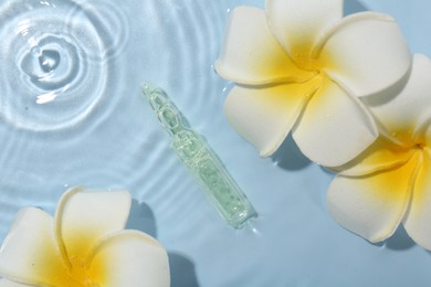 Photo of Skincare ampoule and beautiful plumeria flowers in water on light blue background, flat lay