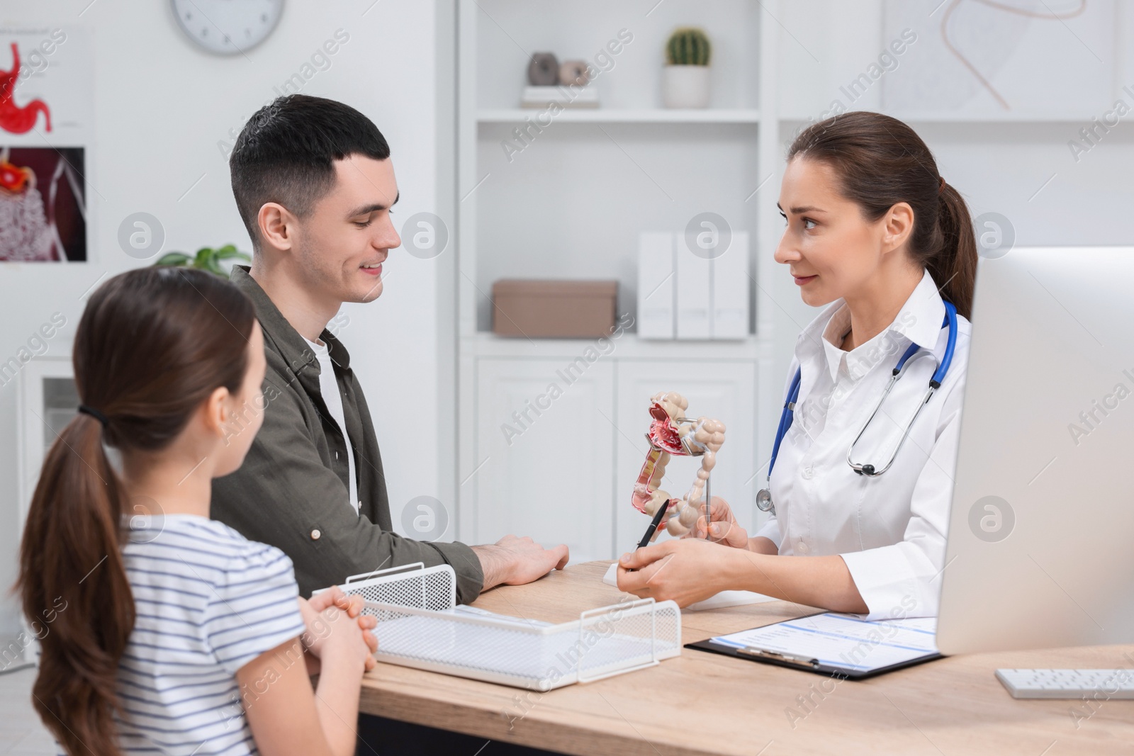 Photo of Gastroenterologist with model of intestine consulting man and his daughter in clinic