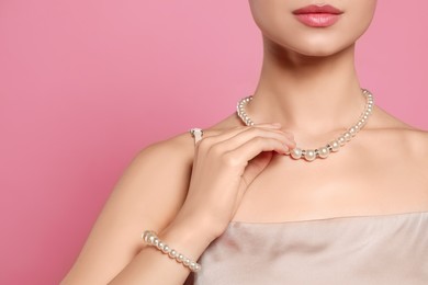 Photo of Young woman wearing elegant pearl jewelry on pink background, closeup. Space for text