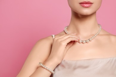 Young woman wearing elegant pearl jewelry on pink background, closeup. Space for text