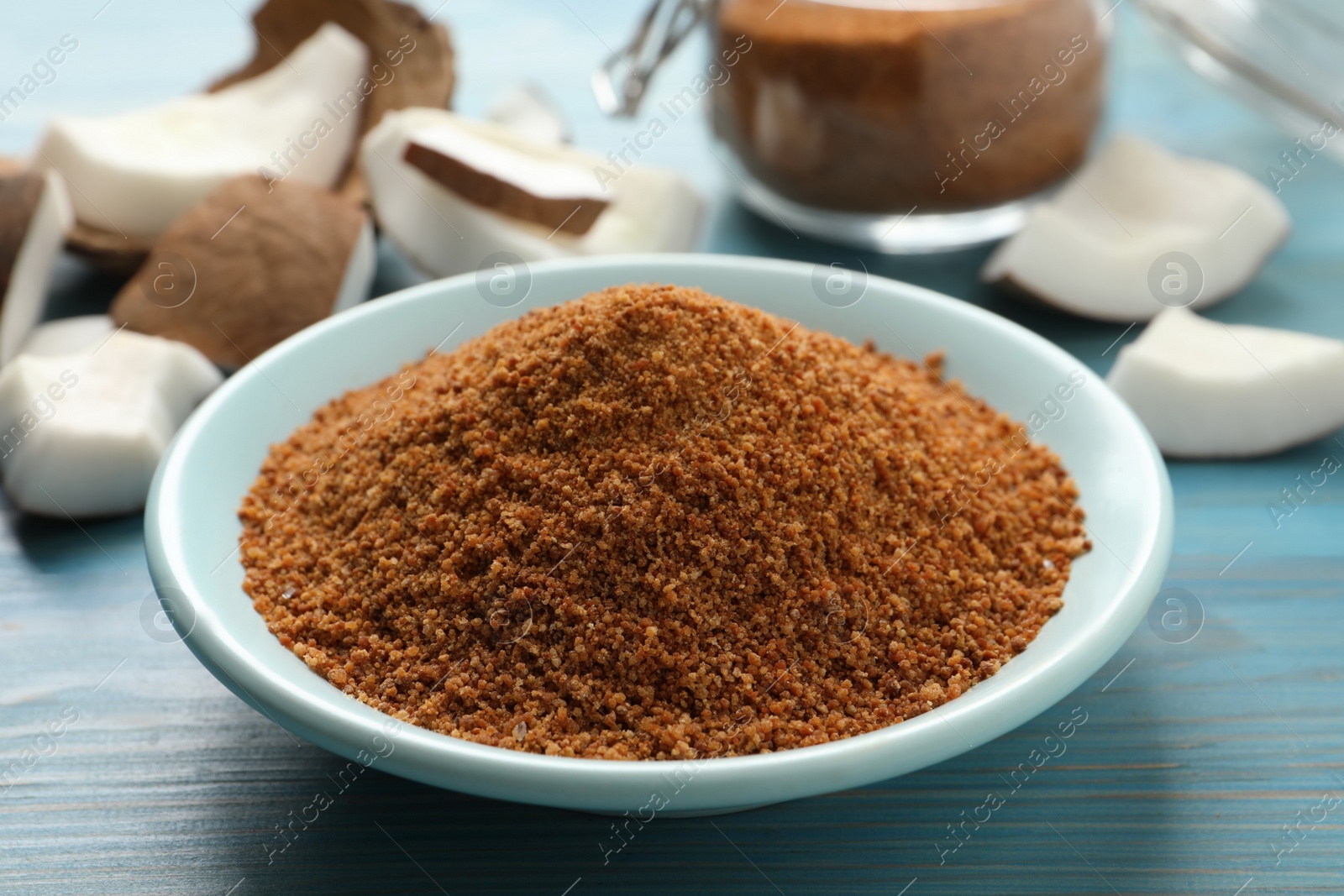 Photo of Natural coconut sugar in ceramic bowl on blue wooden table, closeup