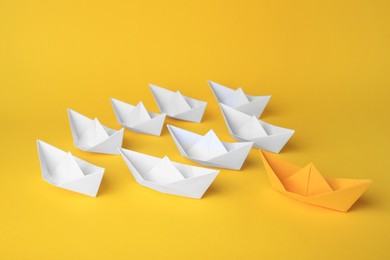 Photo of Group of paper boats following yellow one on color background. Leadership concept