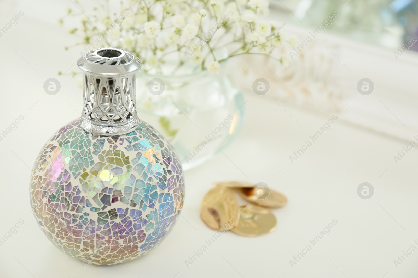 Photo of Closeup view of stylish catalytic lamp with beautiful gypsophila and earrings on white table, space for text. Cozy interior