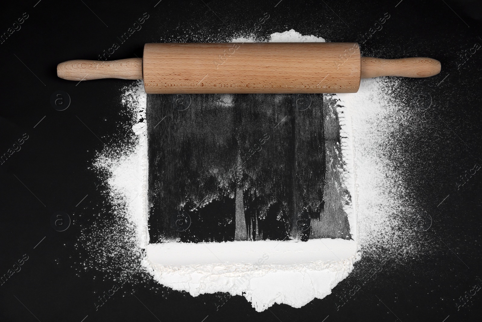 Photo of Flour and rolling pin on black table, flat lay