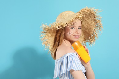 Photo of Beautiful young woman in straw hat with sun protection cream on light blue background, space for text