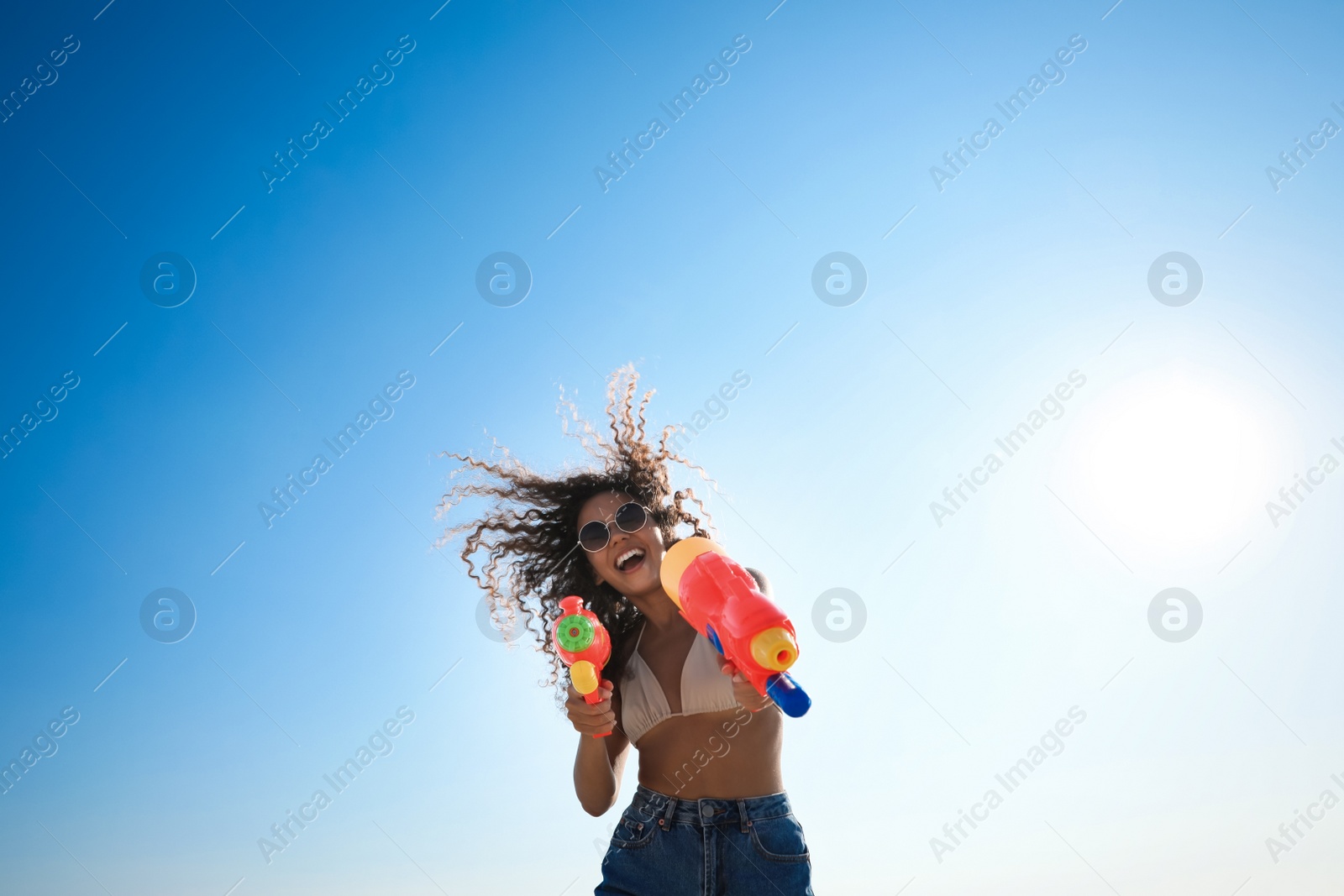 Photo of African American woman with water guns against blue sky, low angle view