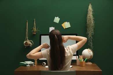 Woman sitting at wooden desk with computer near green wall, back view. . Interior design