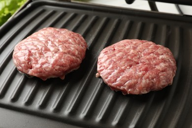 Photo of Fresh raw hamburger patties on electric grill, closeup