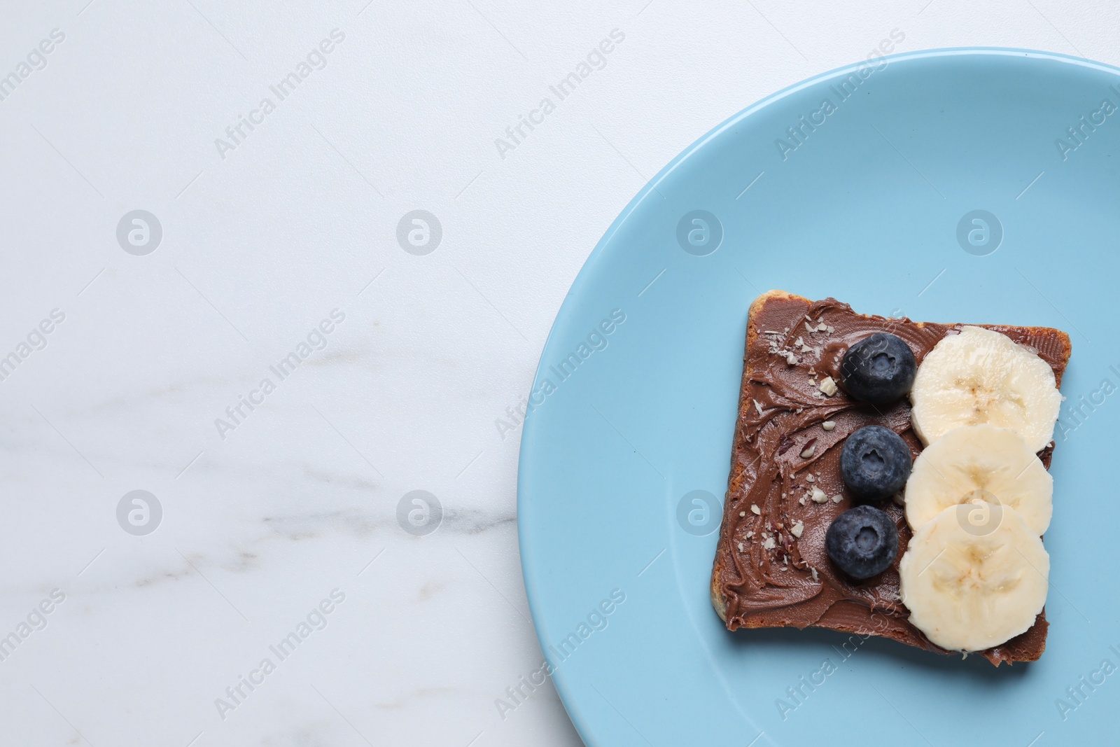 Photo of Toast with tasty nut butter, blueberries, banana and nuts isolated on white marble table, top view. Space for text