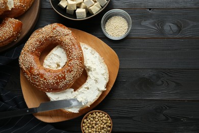 Photo of Delicious bagel with tofu cream cheese and soy beans on black wooden table, flat lay. Space for text