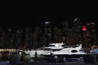 Photo of DUBAI, UNITED ARAB EMIRATES - NOVEMBER 03, 2018: Night cityscape with luxury yachts moored at pier