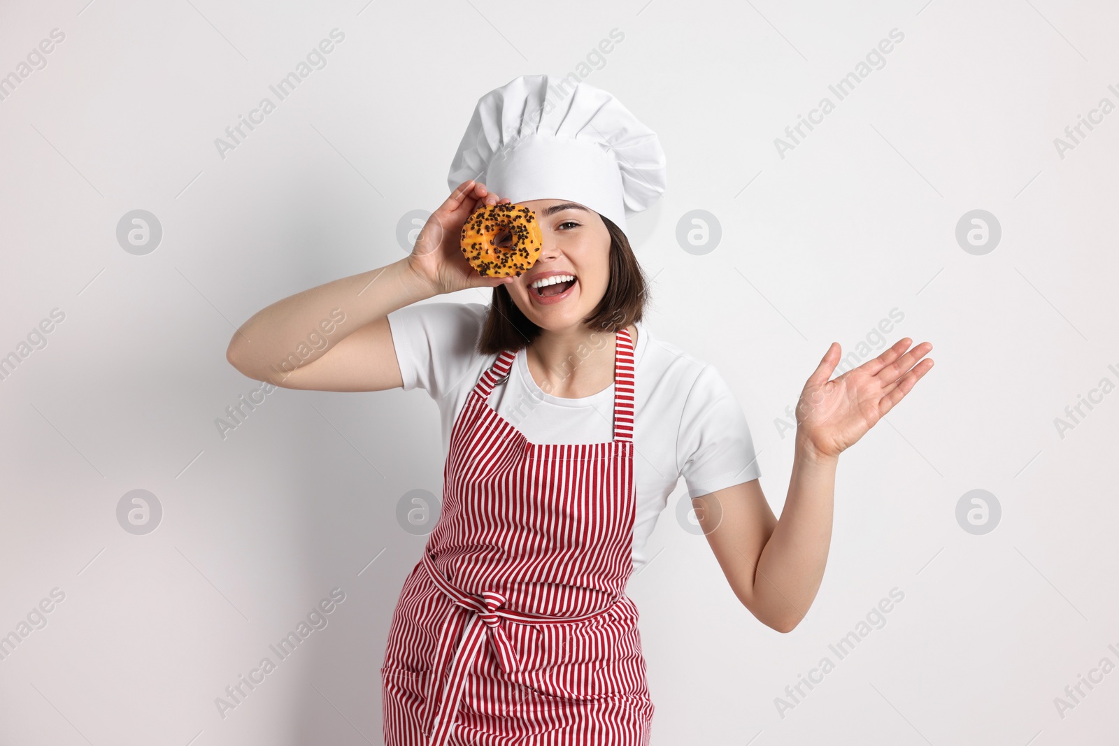 Photo of Happy confectioner with donut on light grey background