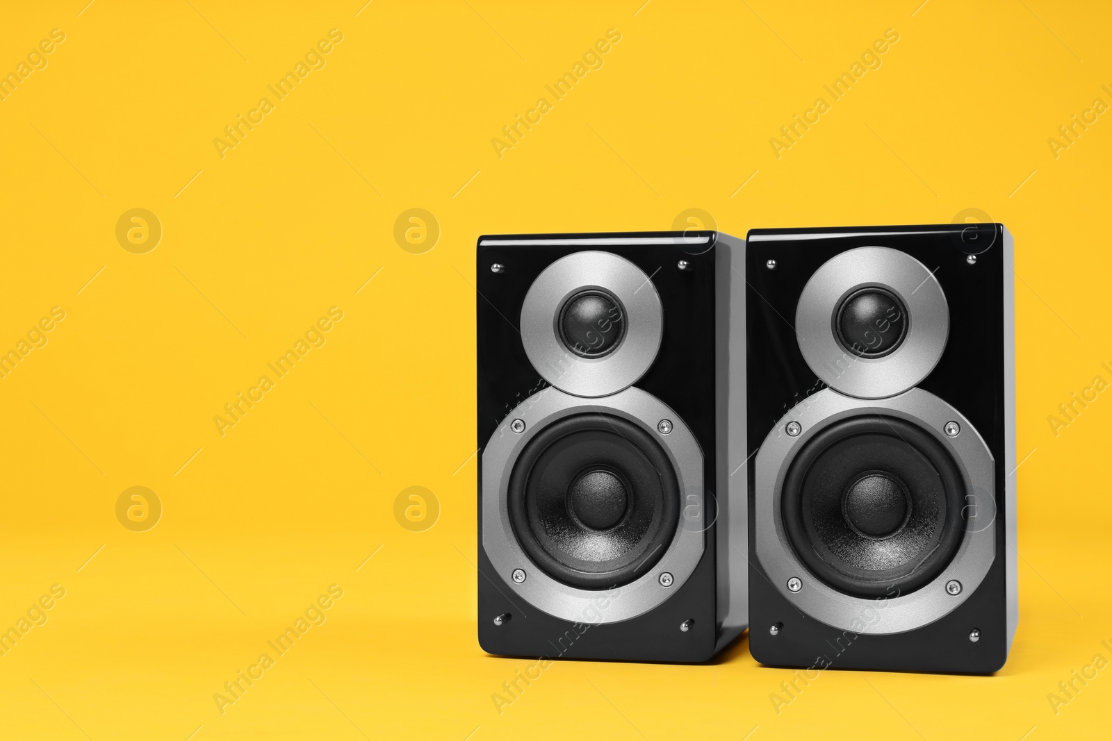 Photo of Modern powerful audio speakers on yellow background, space for text