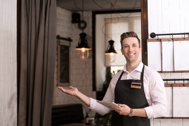 Photo of Young waiter in apron with tablet computer at workplace