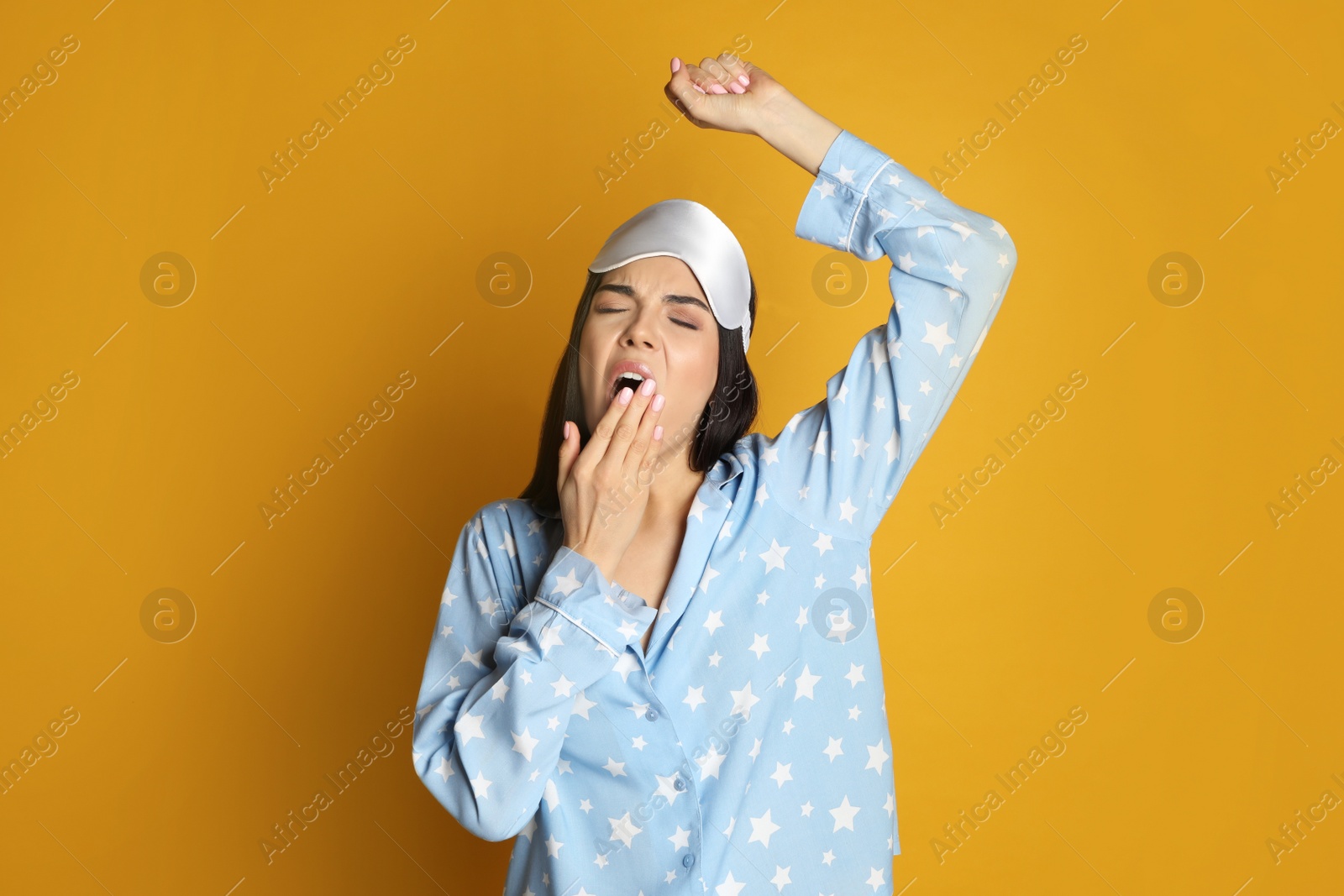 Photo of Young tired woman with sleeping mask yawning on yellow background