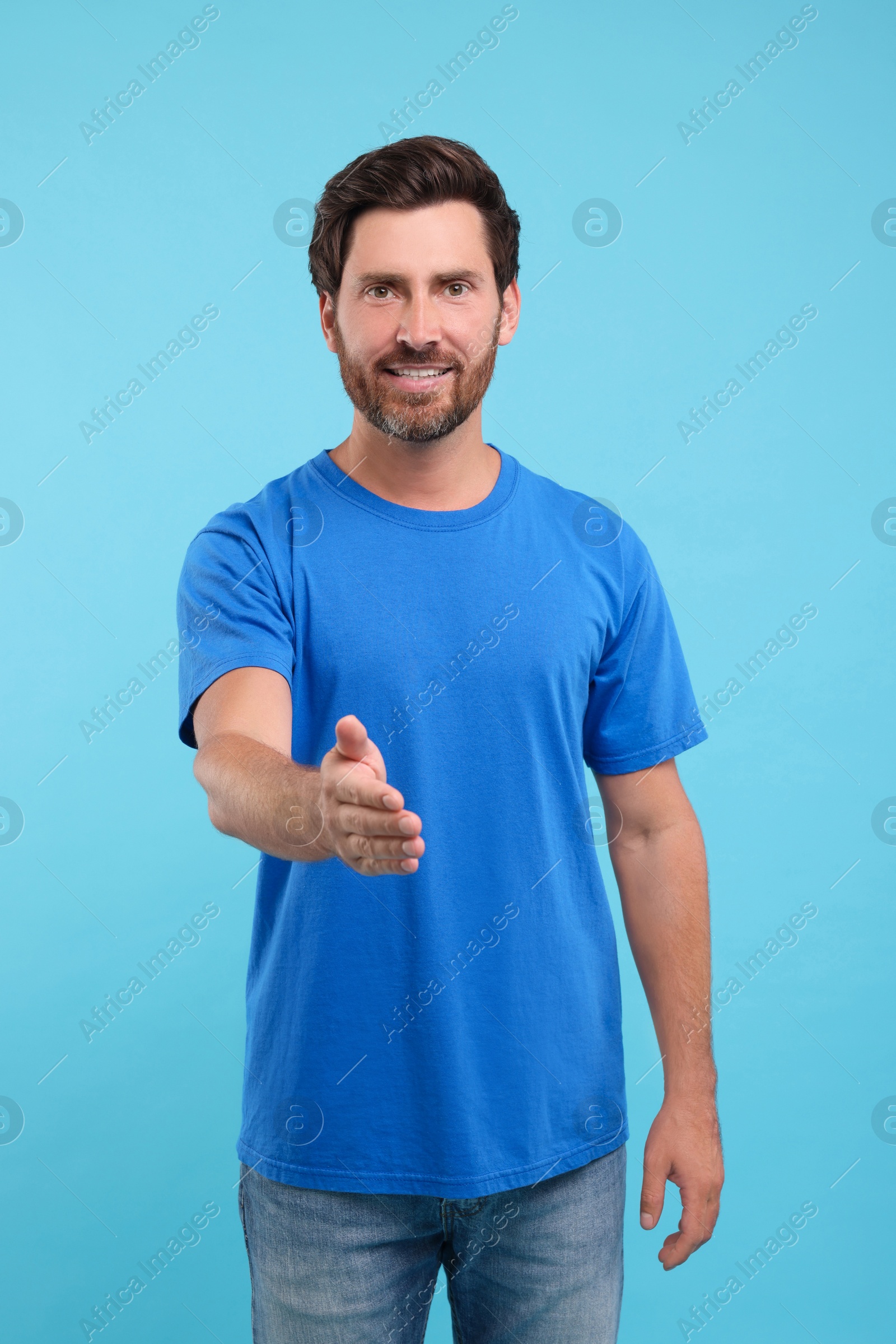 Photo of Happy man welcoming and offering handshake on light blue background