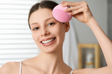 Photo of Washing face. Young woman with cleansing brush indoors