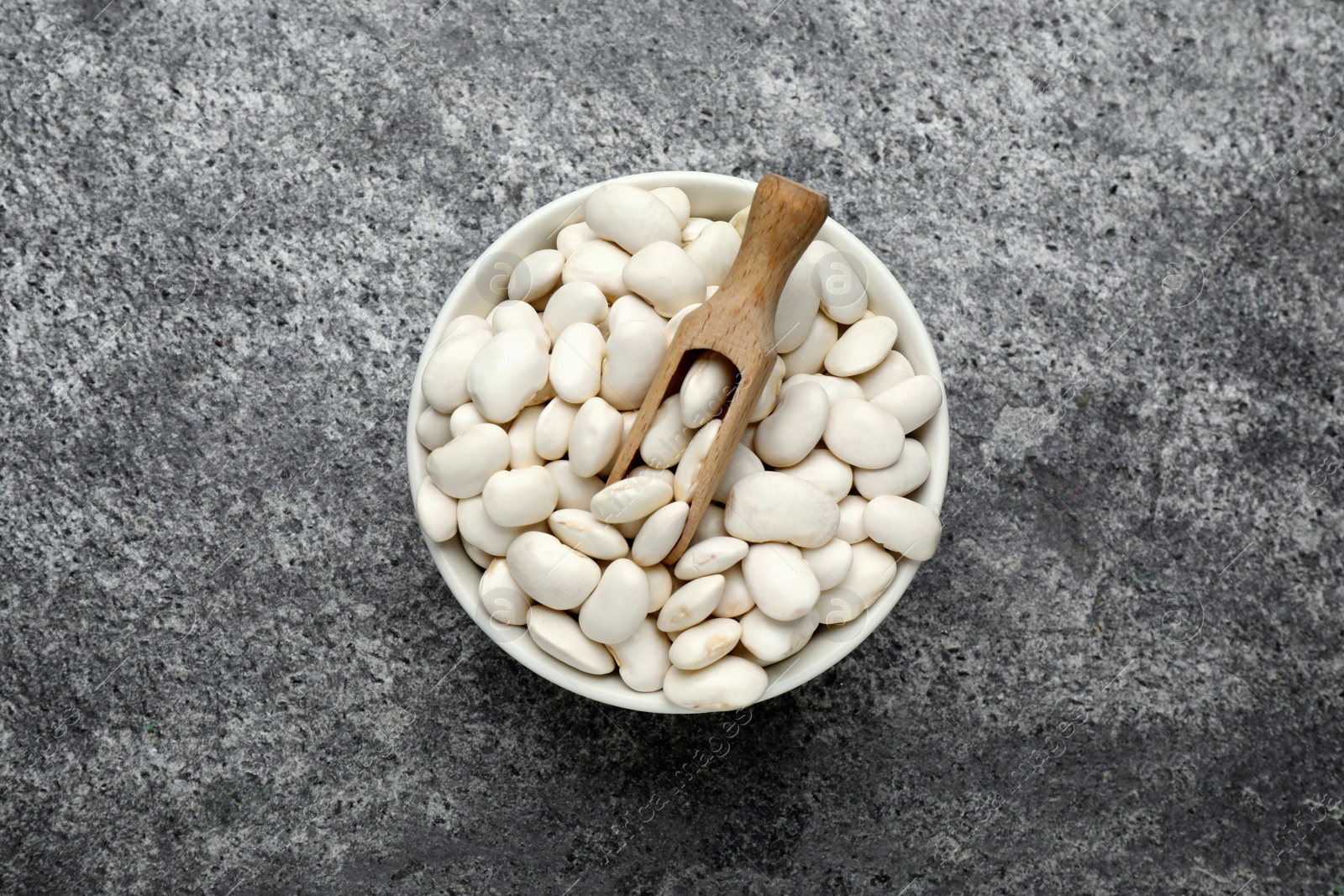 Photo of Raw white beans and scoop in bowl on grey table, top view