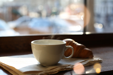 Photo of Delicious morning coffee, newspaper and croissant near window, indoors