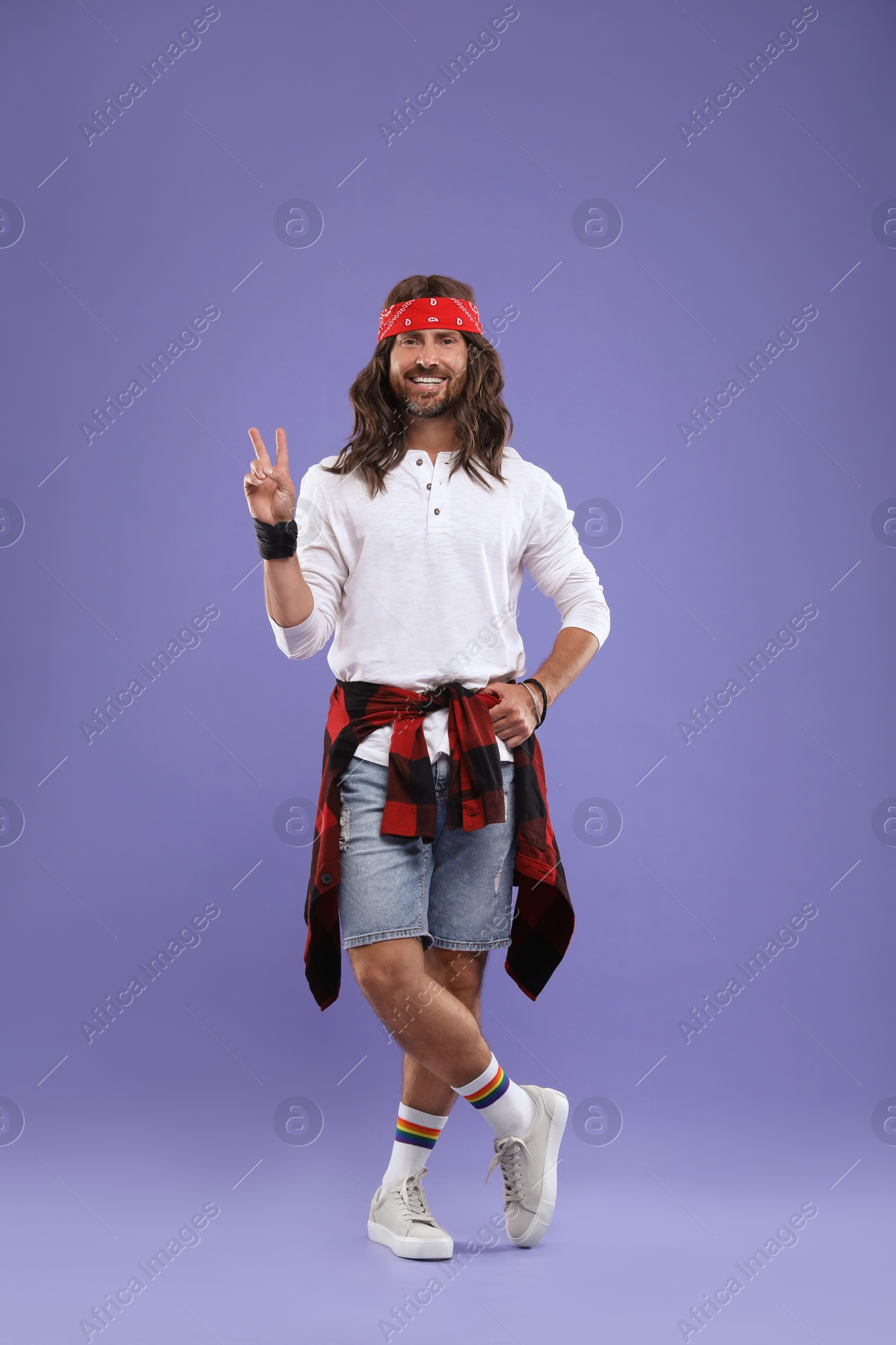 Photo of Stylish hippie man showing V-sign on violet background