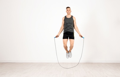 Photo of Full length portrait of young sportive man training with jump rope in light room