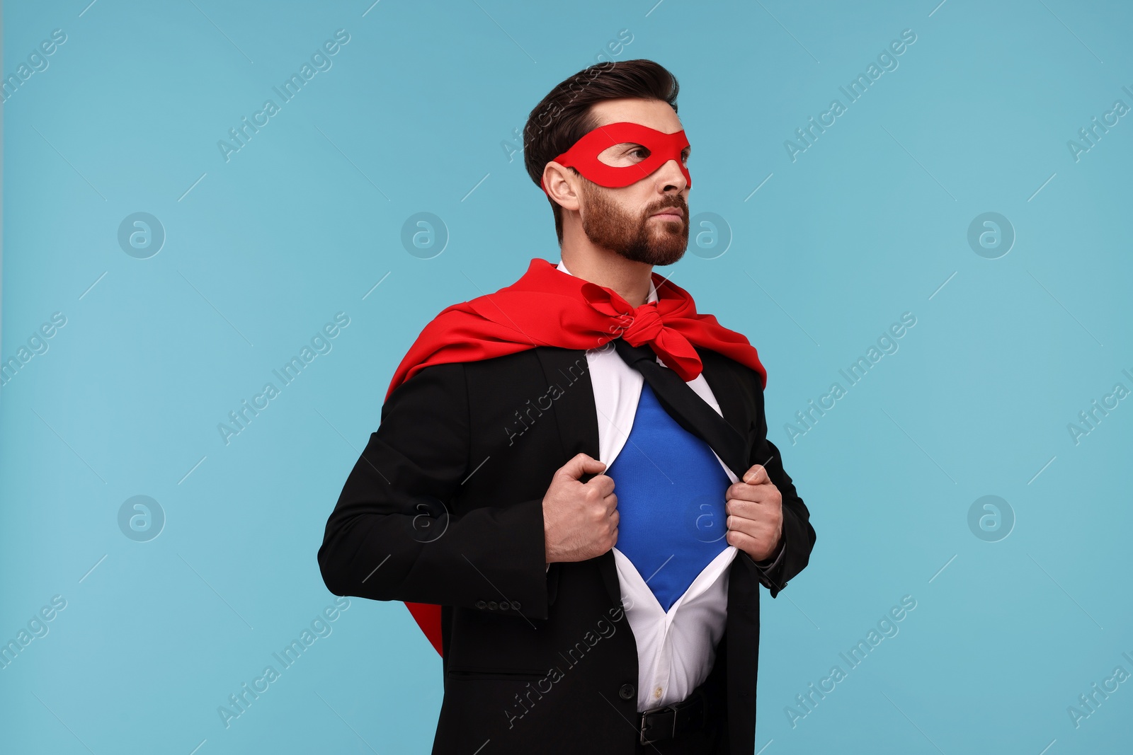 Photo of Confident businessman wearing superhero costume under suit on light blue background