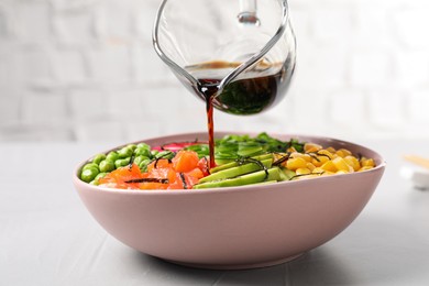 Photo of Adding soy sauce to delicious salad with salmon and vegetables on grey table, closeup