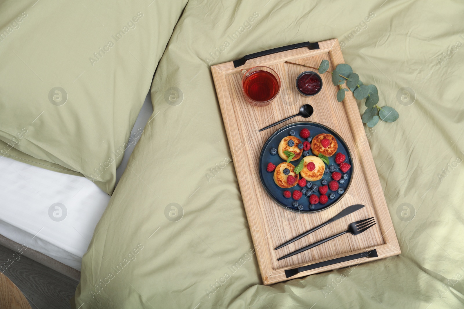 Photo of Tasty breakfast served in bedroom. Cottage cheese pancakes with fresh berries and mint on wooden tray, top view