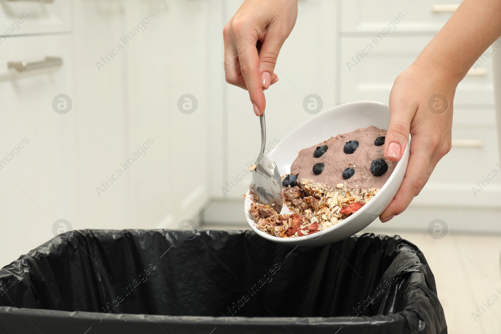 Photo of Woman throwing oatmeal with berries into bin indoors, closeup