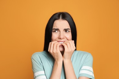 Photo of Young woman biting her nails on yellow background