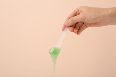 Woman holding spatula with hot depilatory wax on beige background, closeup. Space for text