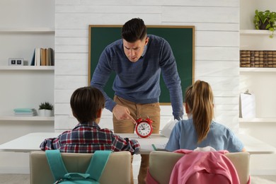 Photo of Teacher with alarm clock scolding pupils for being late in classroom