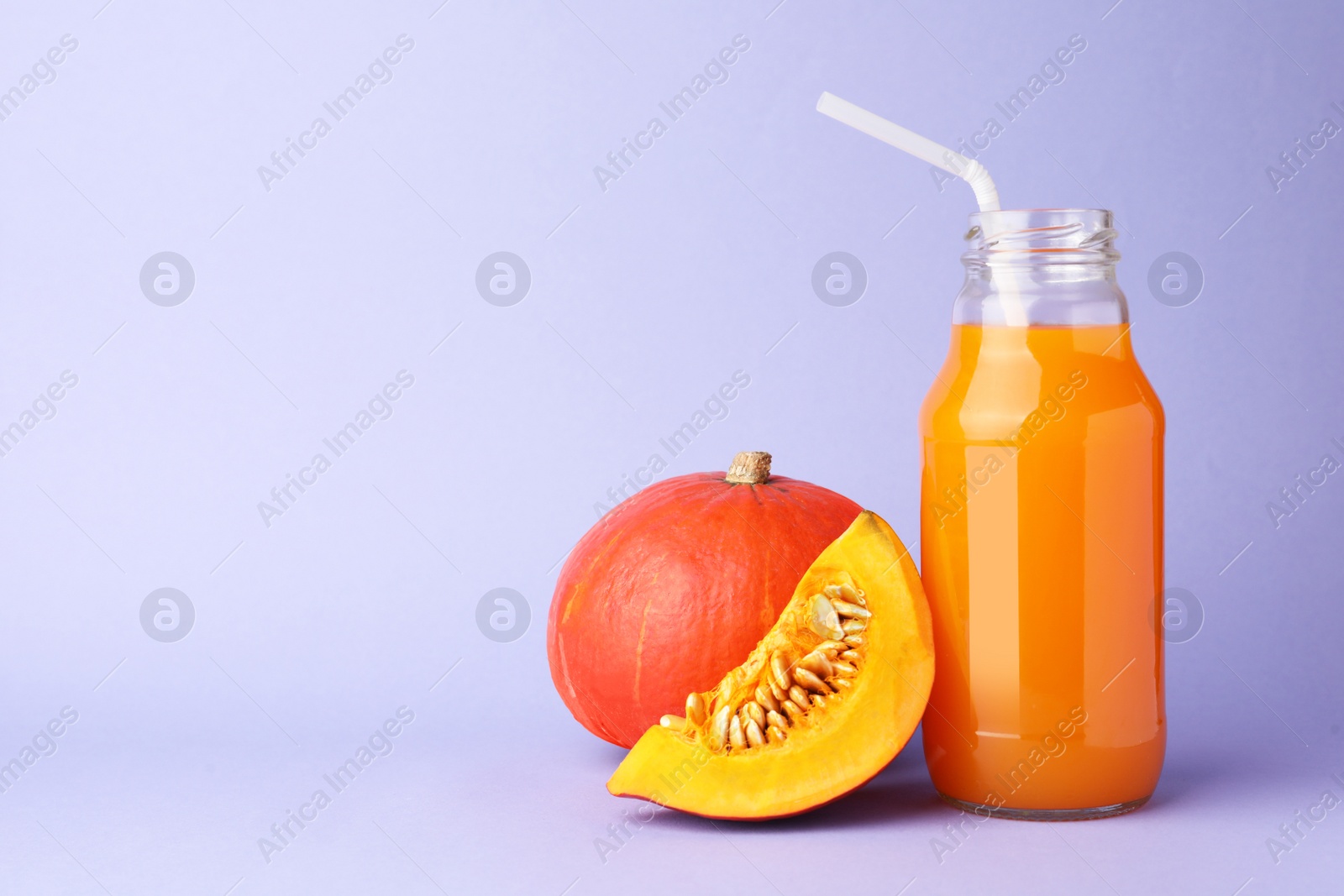 Photo of Tasty pumpkin juice in glass bottle, whole and cut pumpkins on lavender color background, space for text