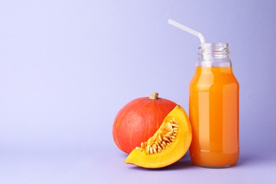 Photo of Tasty pumpkin juice in glass bottle, whole and cut pumpkins on lavender color background, space for text