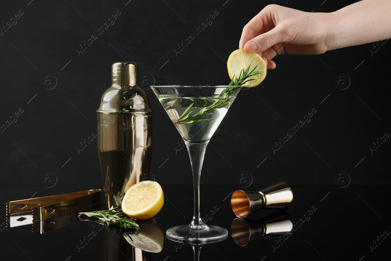 Photo of Woman decorating Martini cocktail with lemon slice on black background, closeup