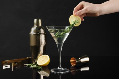 Photo of Woman decorating Martini cocktail with lemon slice on black background, closeup