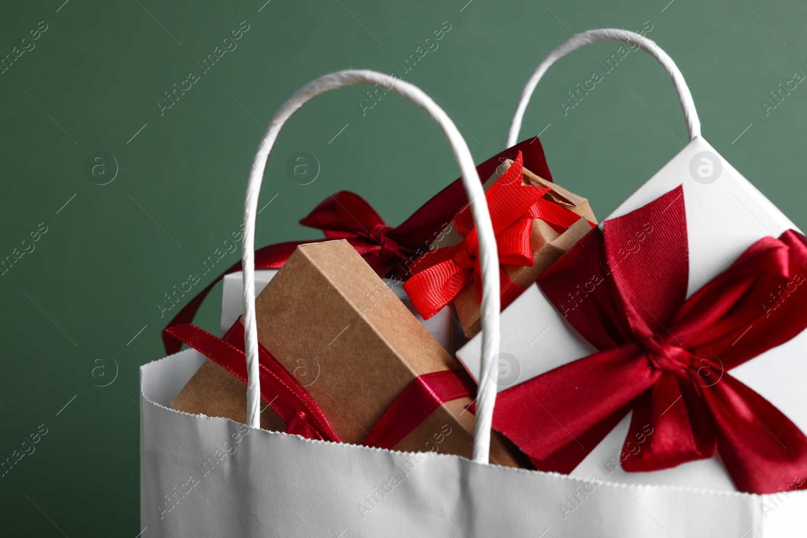 Photo of Turquoise paper shopping bag full of gift boxes on green background, closeup