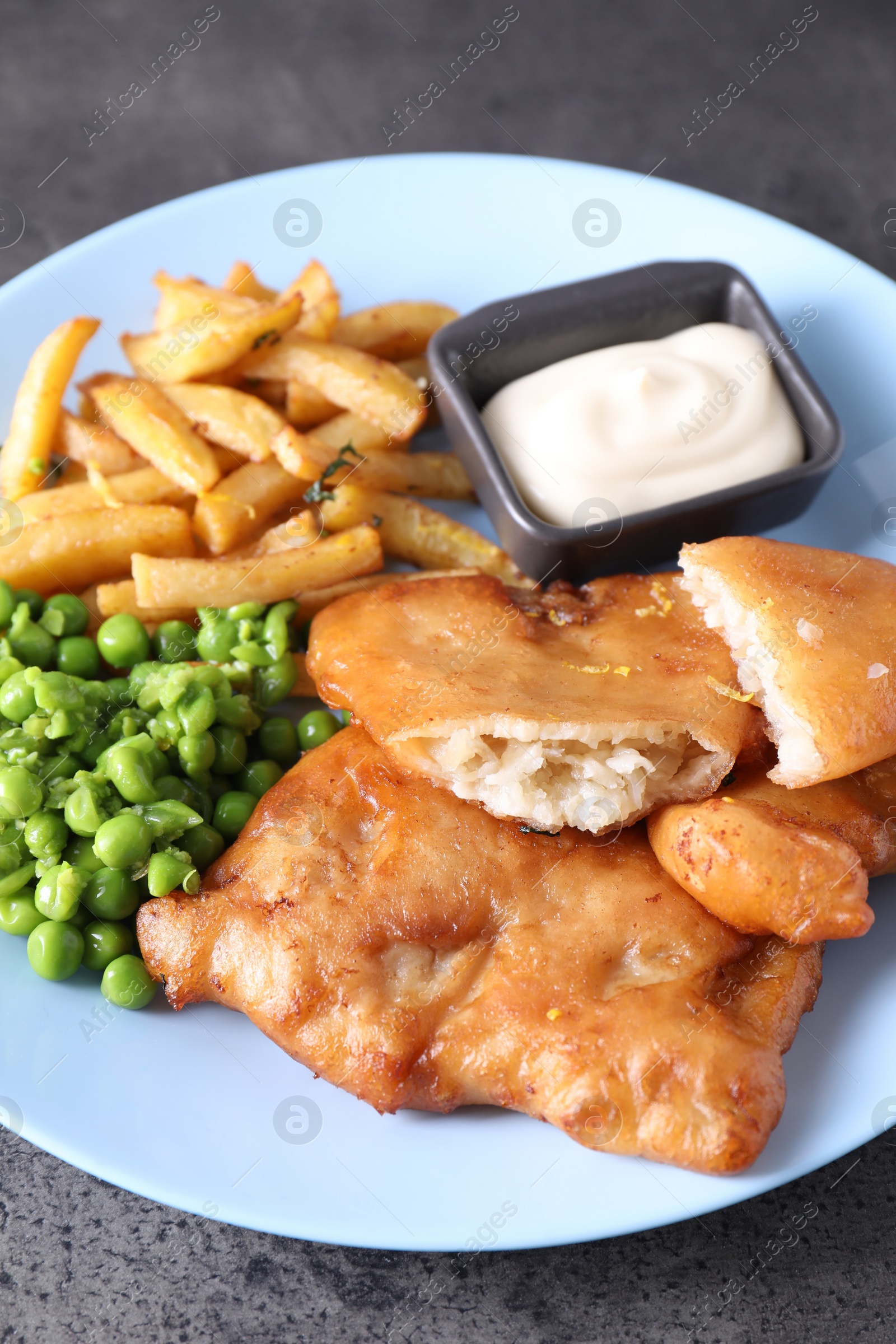 Photo of Tasty fish, chips, sauce and peas on grey table, closeup