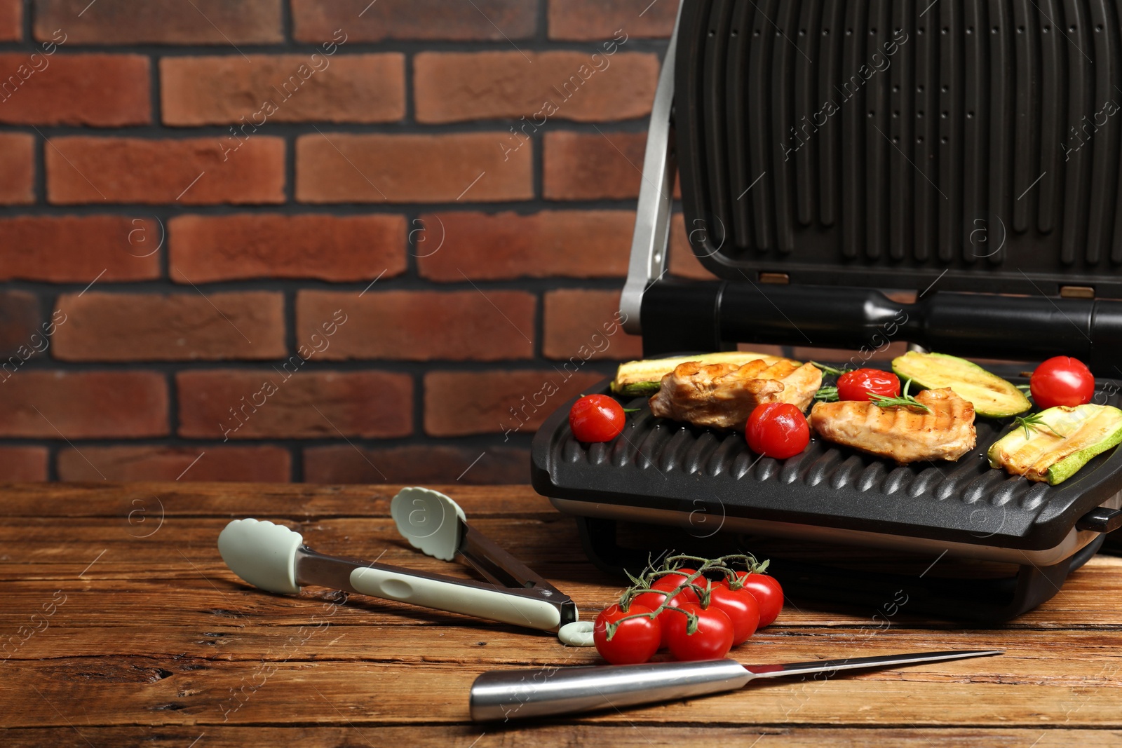 Photo of Electric grill with tasty meat, rosemary and vegetables on wooden table