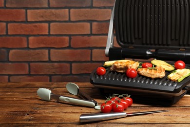 Electric grill with tasty meat, rosemary and vegetables on wooden table