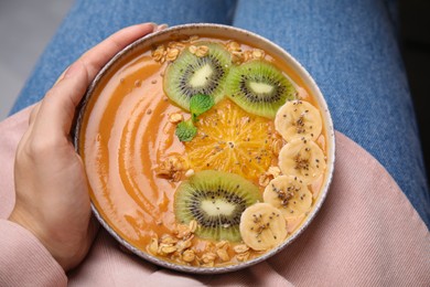 Photo of Woman holding bowl of delicious fruit smoothie with fresh banana, kiwi slices and granola, top view