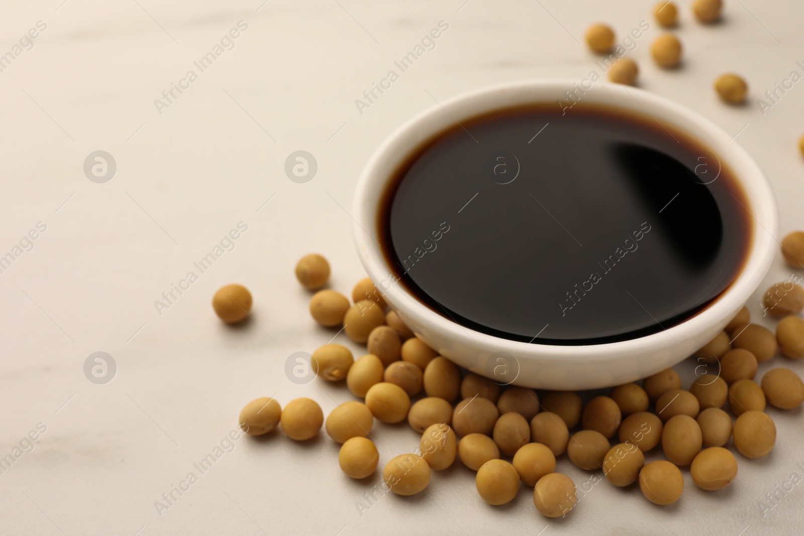 Photo of Soy sauce in bowl and soybeans on white table, closeup. Space for text
