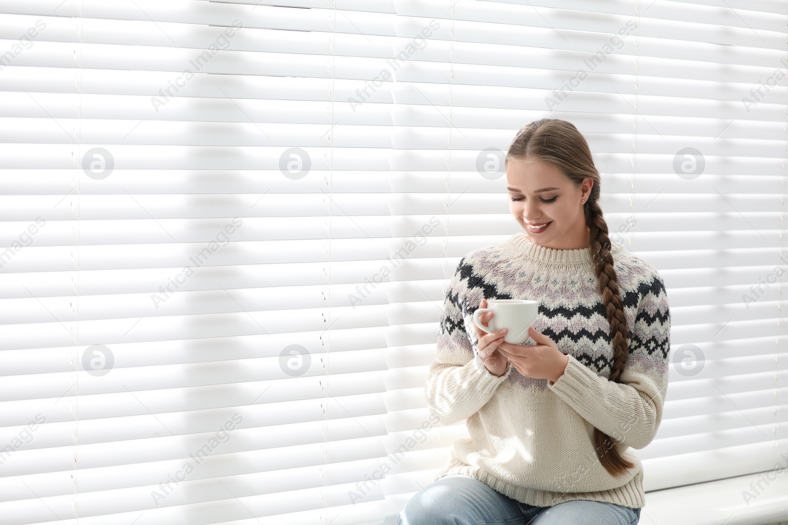 Photo of Young woman with hot drink near window at home