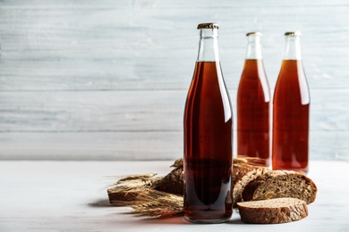 Photo of Bottle of delicious fresh kvass, spikelets and bread on white wooden table. Space for text