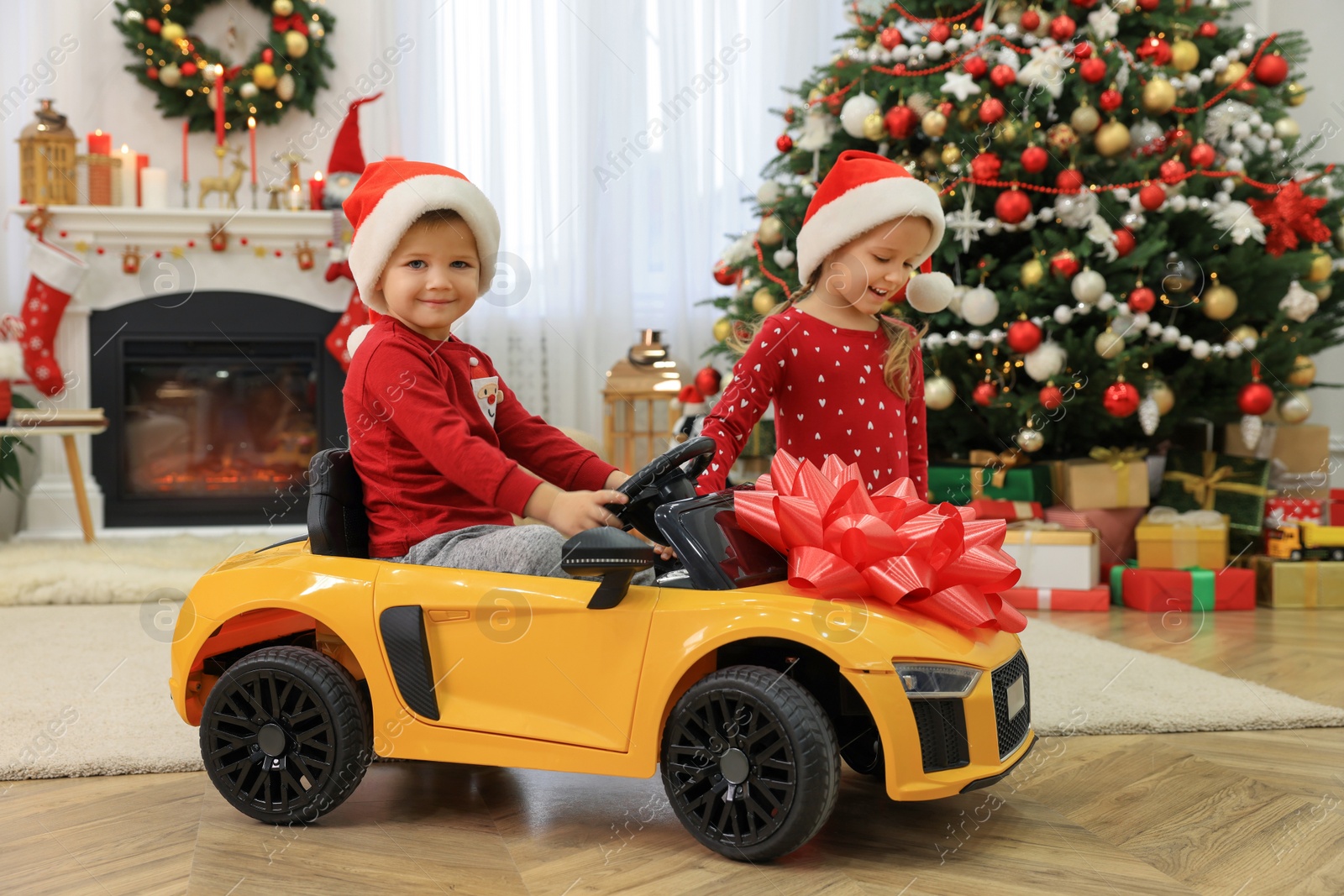 Photo of Cute little children playing with toy car in room decorated for Christmas