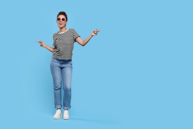 Photo of Happy young woman in sunglasses dancing on light blue background. Space for text